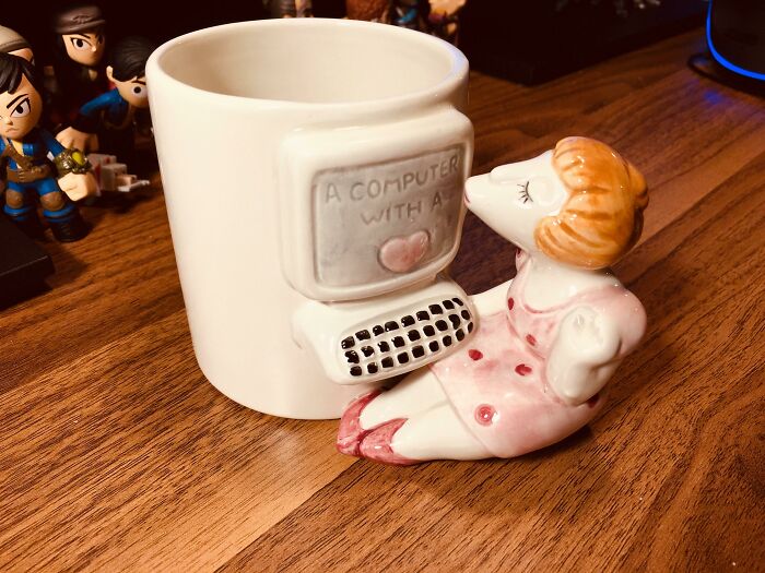 A white mug with a ceramic woman kissing a computer, among unhinged secondhand finds.