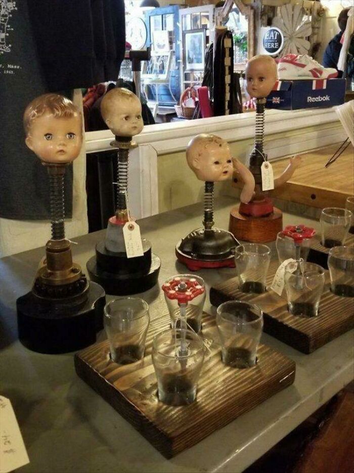 Four disturbing doll head sculptures mounted on springs and metal bases, next to several glasses, among unhinged secondhand finds.
