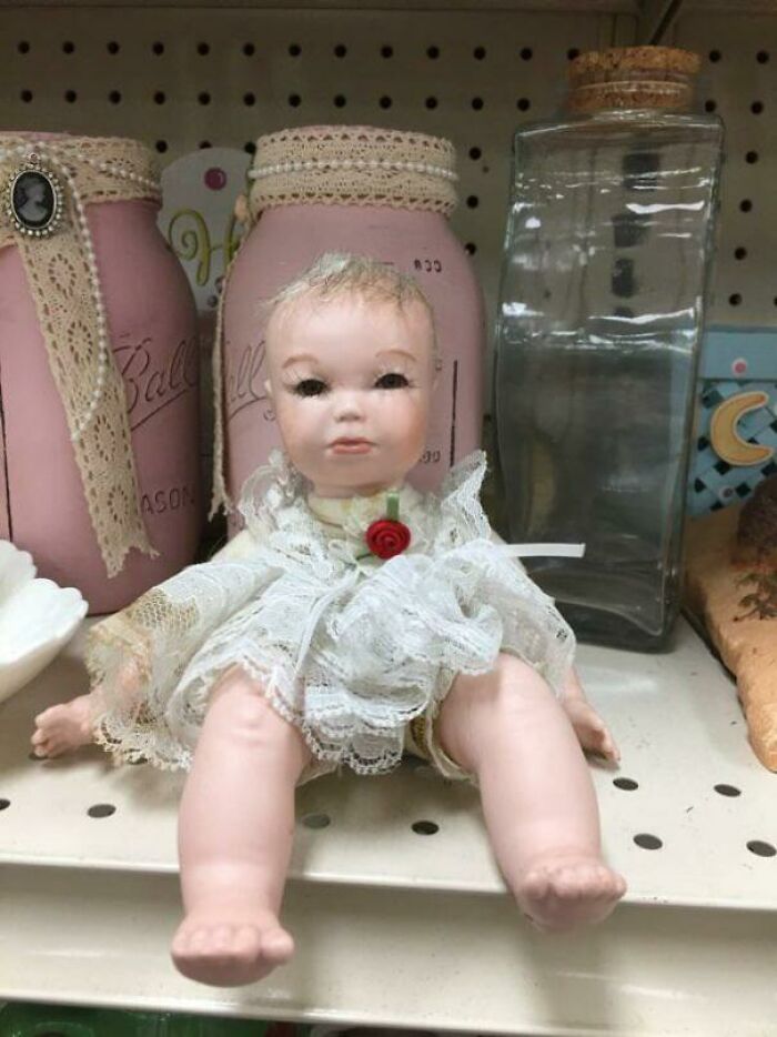 A small, antique-looking baby doll with a lace outfit, a strange unhinged secondhand find on a shelf.