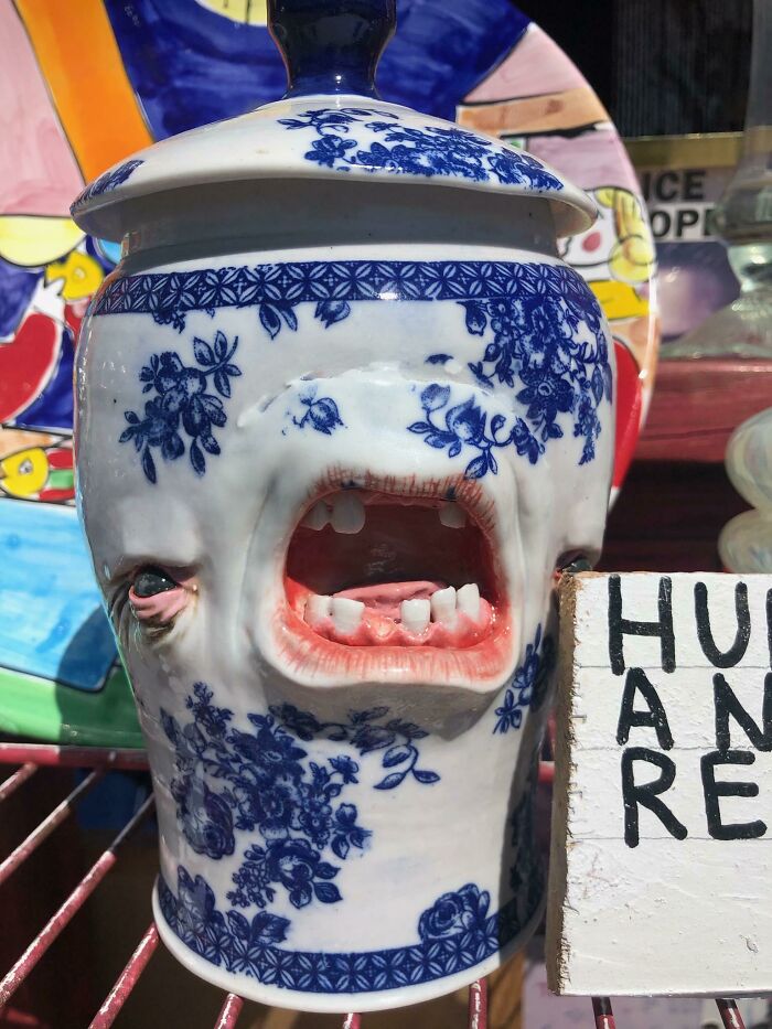 A white and blue floral ceramic jar with a grotesque face featuring an open mouth and teeth, a cursed secondhand treasure.
