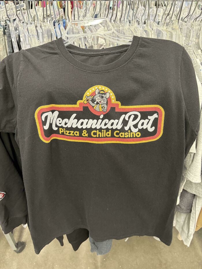 A black T-shirt hanging on a rack with a humorous Mechanical Rat Pizza & Child Casino logo, a unique secondhand find.