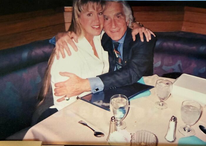 A couple embracing at a table, sharing a wild delayed plot twist from life.