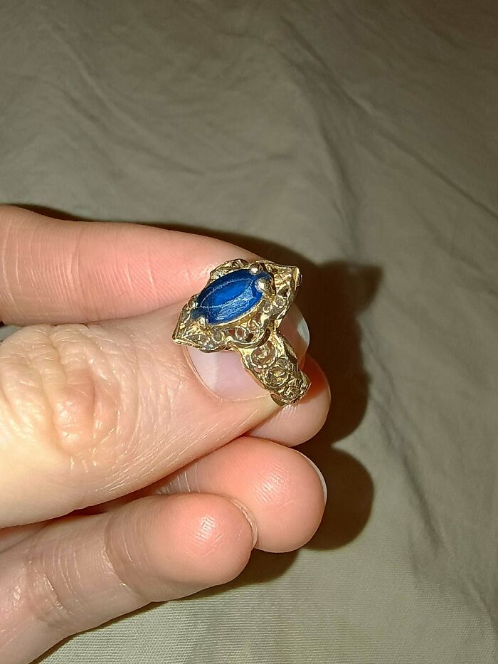 A hand holding a remarkable antique gold ring with a striking blue gemstone, highlighting its unique design.