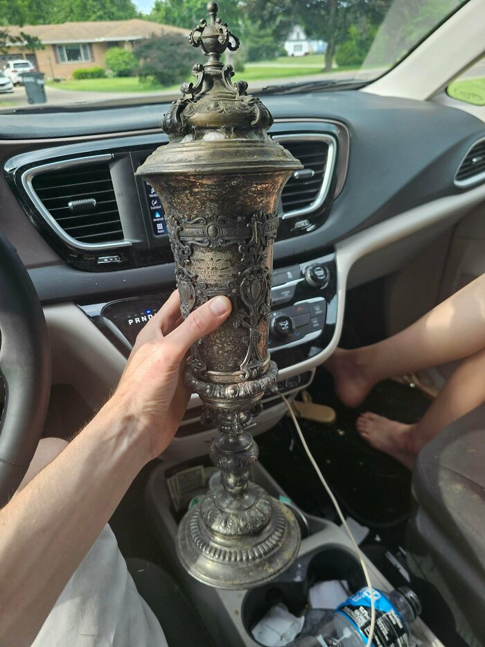 A person holding a remarkable antique ornate silver vase-like object inside a car, showcasing its intricate details.