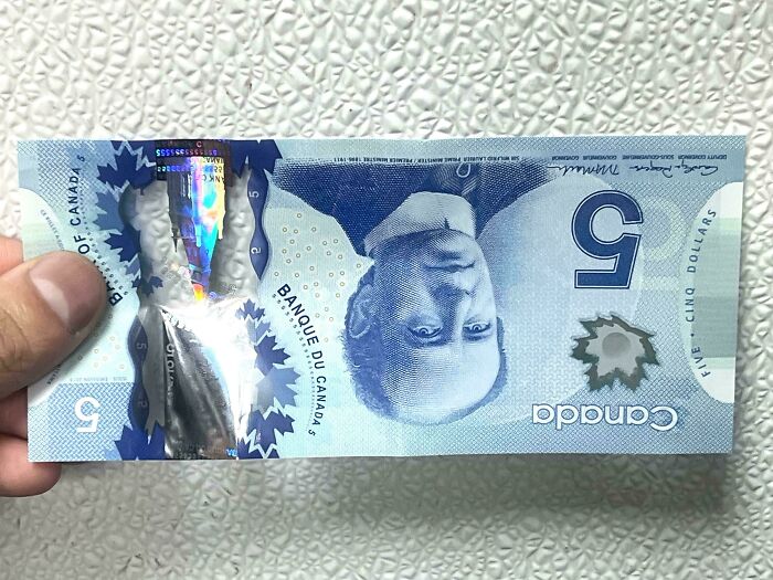 A hand holds a Canadian five-dollar bill upside down, demonstrating online lies.