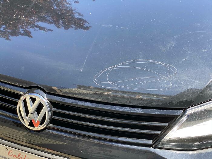 Mischievous kids scratched the hood of a black Volkswagen, showing circular marks.