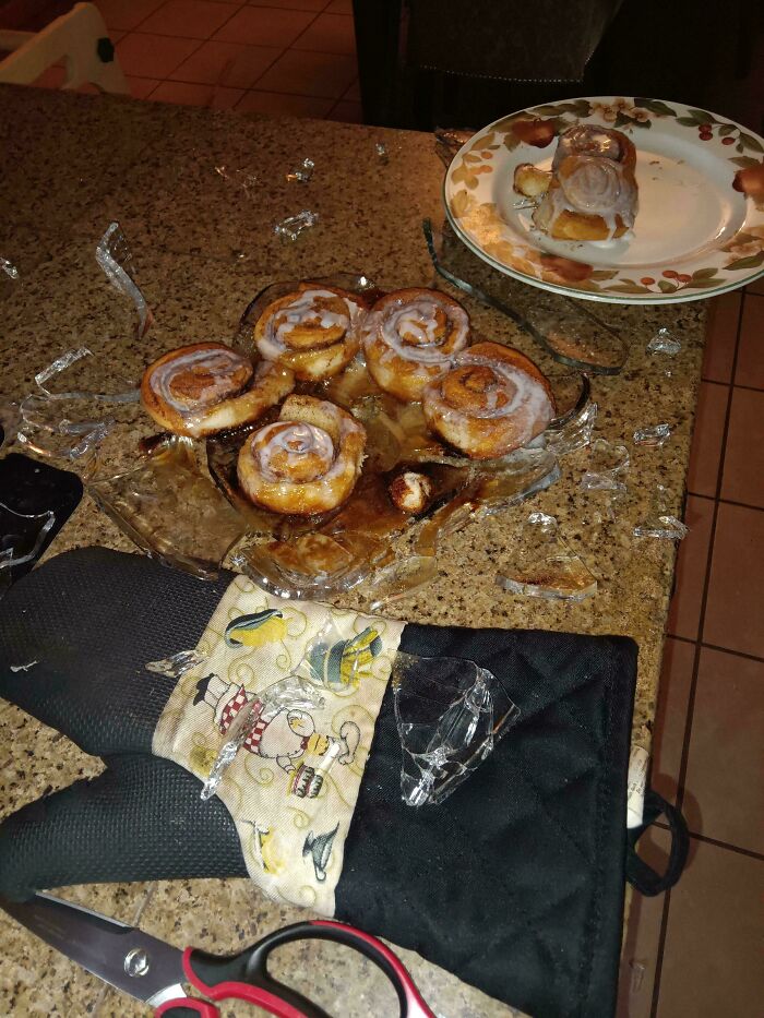 Broken glass and cinnamon rolls scattered on a kitchen counter, a clear sign of mischievous kids' antics.