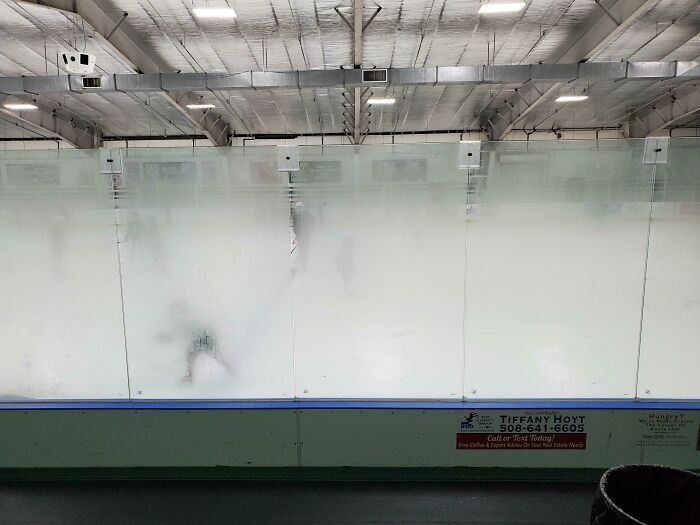A hockey rink with fogged-up glass barriers, suggesting the lively and mischievous kids playing within.