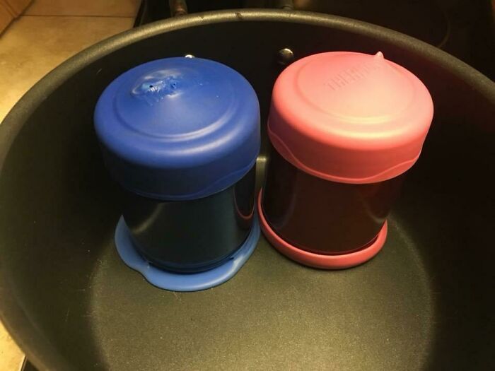 Two covered containers, one blue and one pink, sitting in a black pot, for mischievous kids' meals.