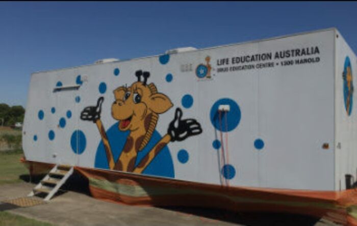 A white Life Education Australia trailer with a smiling giraffe logo giving a thumbs up. A memorable Aussie education experience.