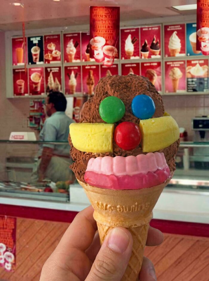 A hand holding a chocolate ice cream cone decorated with candies to look like a face, a fun treat bringing back Aussie memories.