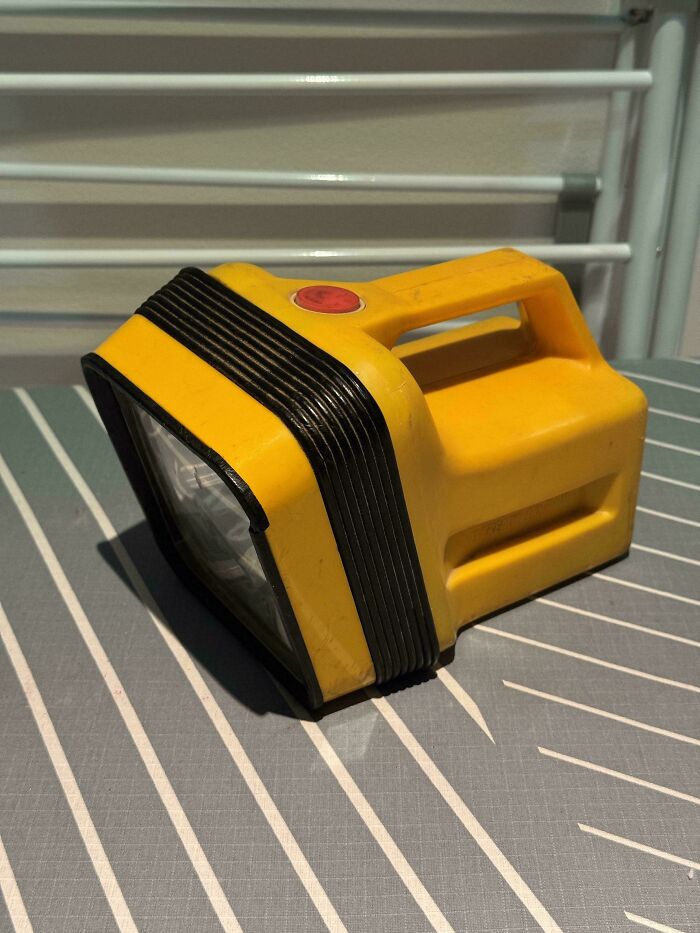 A vintage yellow and black rectangular flashlight with a red button on top, on a striped tablecloth, an Aussie memory.