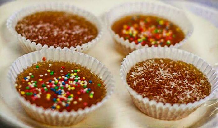 Four individual brown jelly cups in white paper liners, two with colorful sprinkles, two with coconut. A sweet Aussie memory.