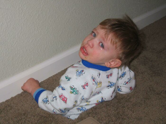 A crying toddler, wearing pajamas, half-submerged in the carpet, showing a moment of mischievous kids.