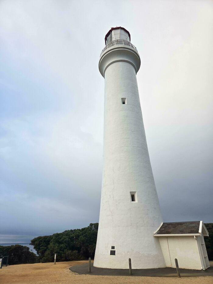 Tall white lighthouse against an overcast sky, reminding of nostalgic Aussie memories.