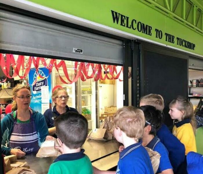 Children line up at a school tuckshop with a sign saying Welcome to the Tuckshop, a nostalgic Aussie memory.