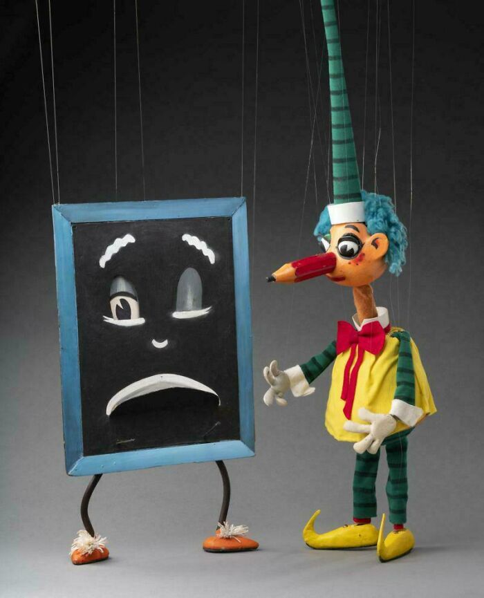 A vintage puppet resembling a boy with a pencil nose next to a sad chalkboard, a nostalgic Aussie memory.