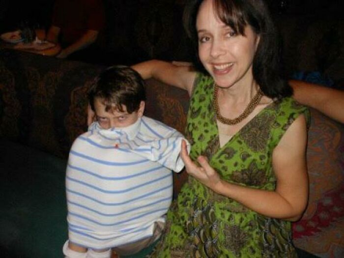 Mischievous kid with a shirt pulled over his head, next to a smiling woman, making parents laugh.