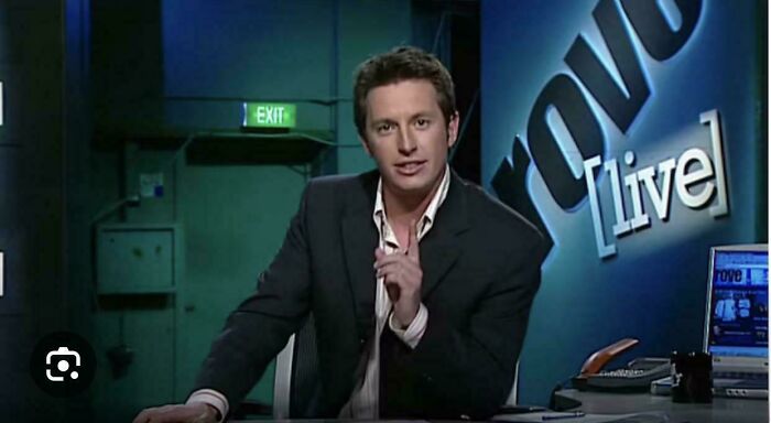 A man in a suit speaking at a desk with Rove Live on the screen, a nostalgic Aussie memory of television.