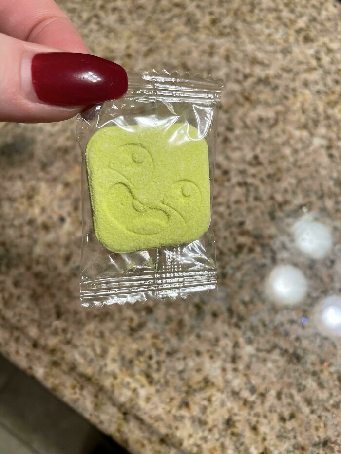 A hand holding a small green packaged candy, a mischievous kids' snack.