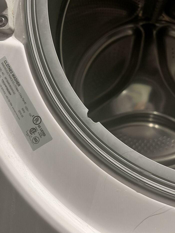 A close-up of a washing machine door with a torn rubber seal, likely from mischievous kids.