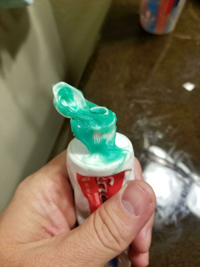 A hand holds a tube of toothpaste with a green, messy dollop squeezed out, showing a mischievous kid's mess.