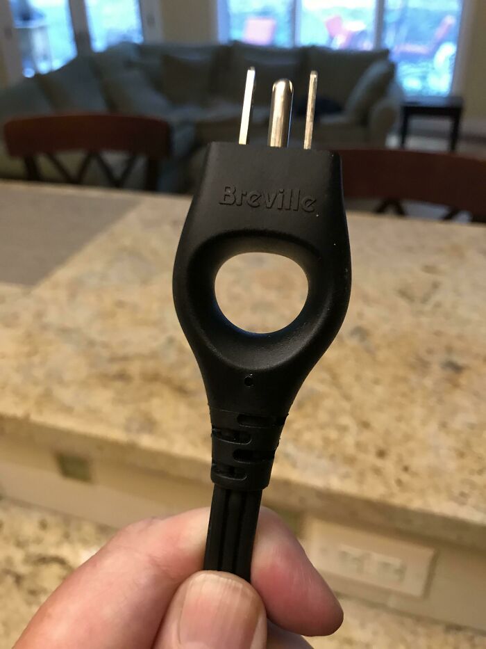 A hand holding a black Breville power plug with a finger hole, an innovative and practical product design.