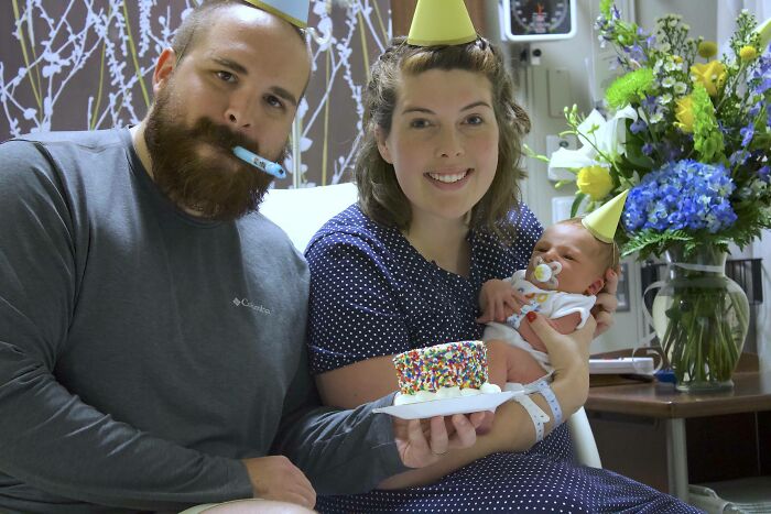 Smiling parents with their newborn, all wearing party hats, celebrating with a small cake, showcasing practical product designs.