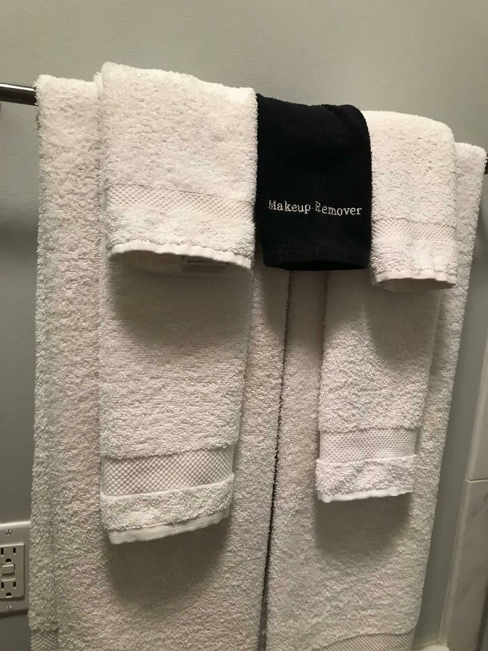 A hotel towel rack with white towels and a black towel labeled Makeup Remover, a practical product design for guests.