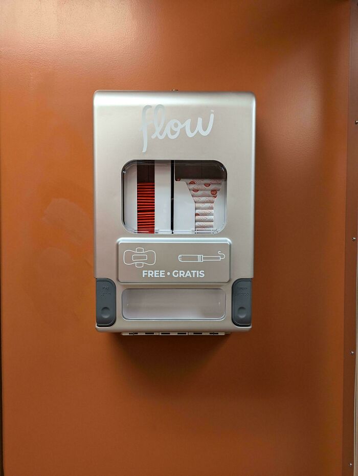 A dispenser on an orange wall offering free feminine hygiene products, showcasing practical product designs for public restrooms.