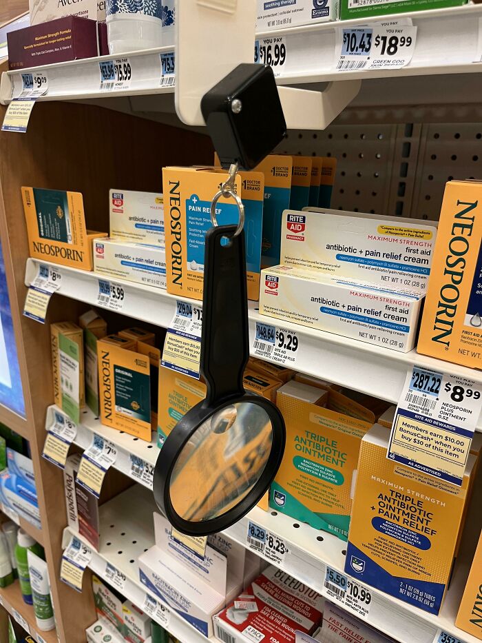 A magnifying glass attached to a shelf in a pharmacy next to Neosporin, a brilliantly practical product design for reading labels.