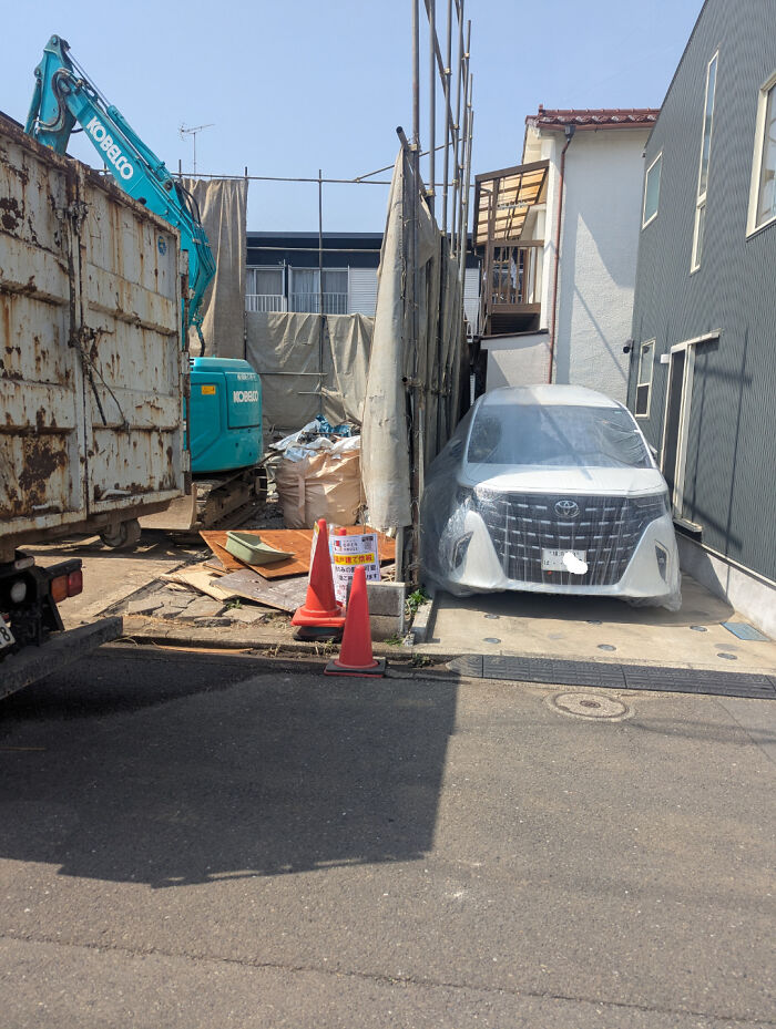 A white car covered in protective plastic next to construction, illustrating a practical product design for protection.