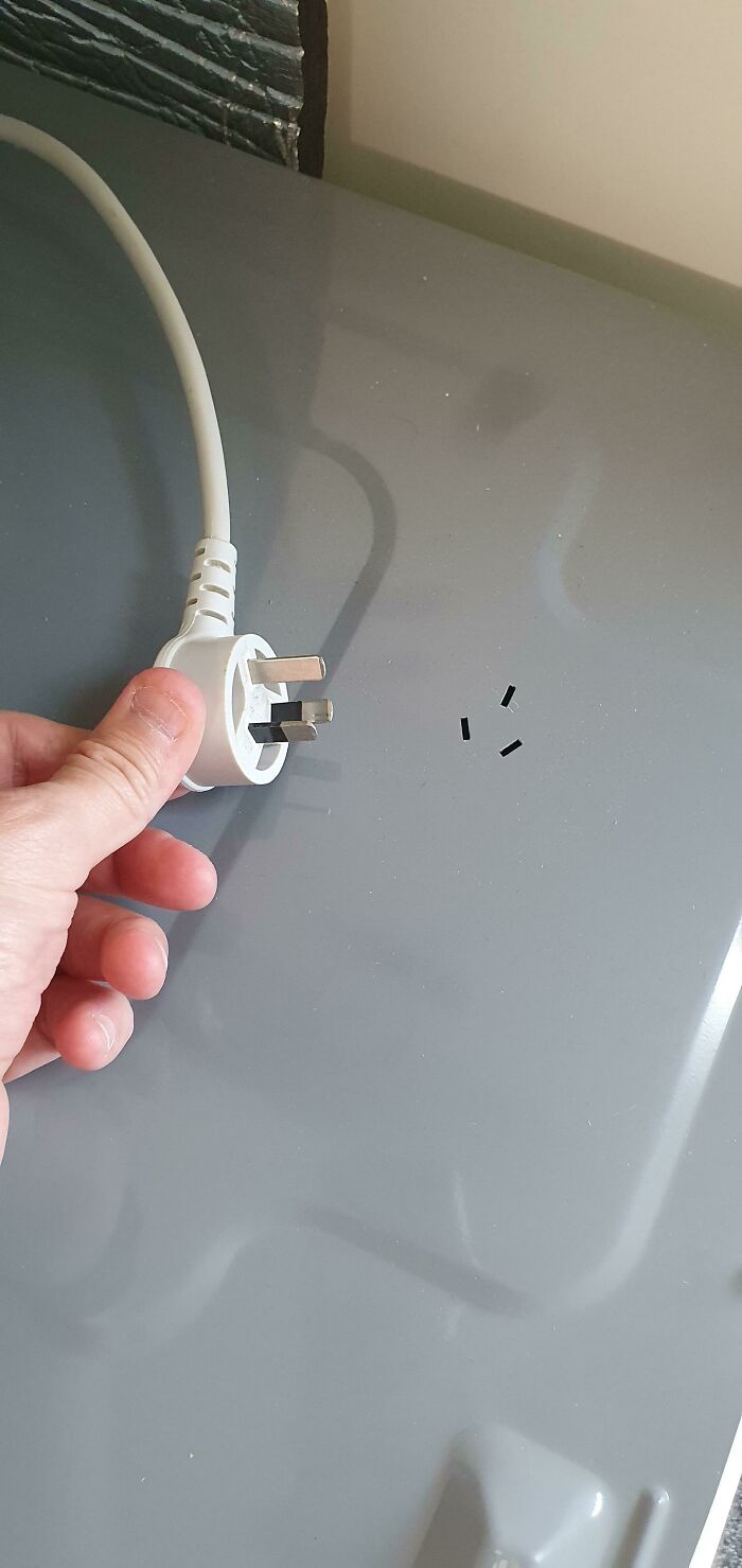 A hand holds a UK plug next to tiny pieces of plastic, a brilliant product design detail for safety.