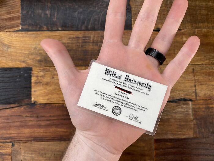 A hand holding a tiny Wilkes University degree, a brilliantly practical product design for a novelty item or gift.