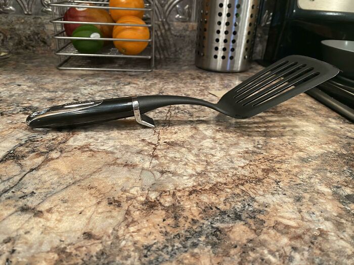 A black and silver spatula with a small stand, showing a practical product design on a marbled countertop.