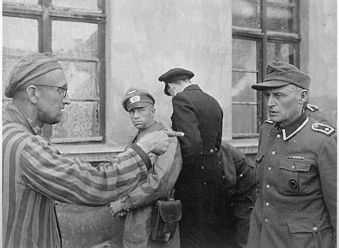A prisoner in striped uniform pointing at a soldier, an impactful image among the historical photos.
