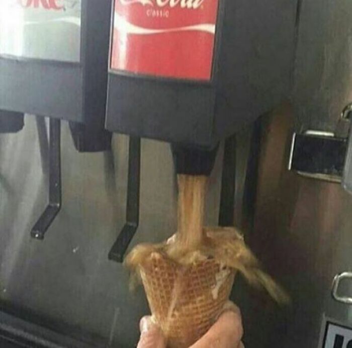 A hand holding an ice cream cone under a soda dispenser, creating an unhinged image.