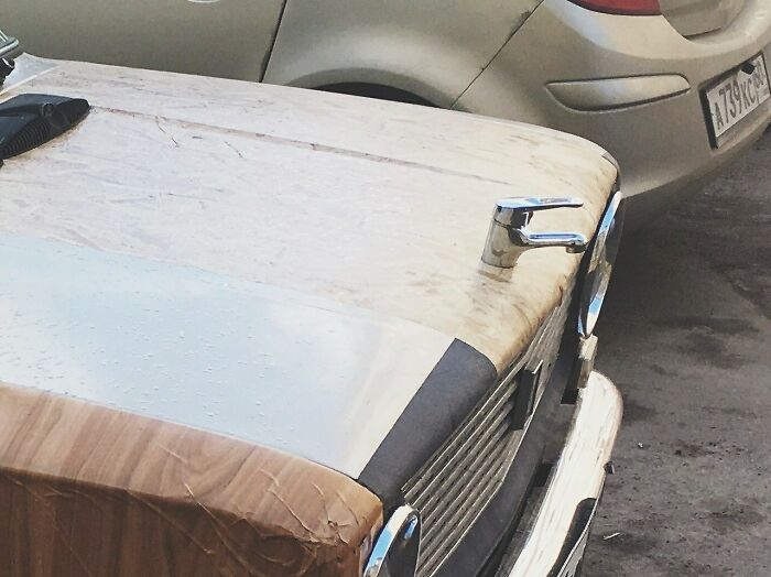 A car with a faucet on its hood and wood-patterned tape, an unhinged image of car customization.
