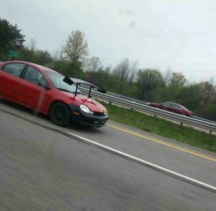 A red car with a large spoiler on its hood, an unhinged image seen on the road.