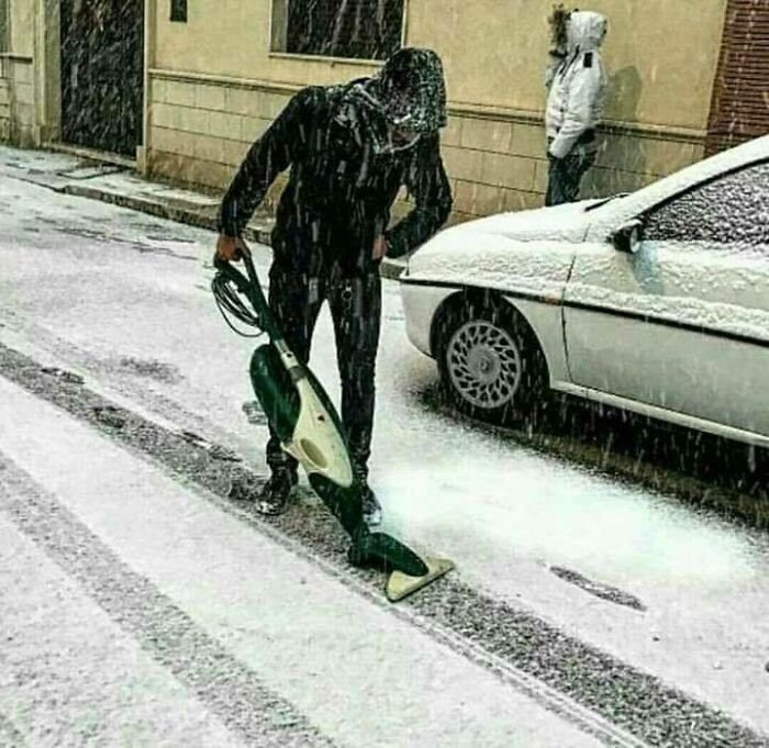 A person vacuuming snow off a sidewalk, an unhinged image that makes people go 'hmmm'.