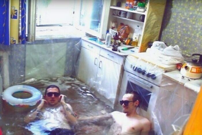 Two men relaxing in a flooded kitchen, showcasing an unhinged image of unexpected leisure.