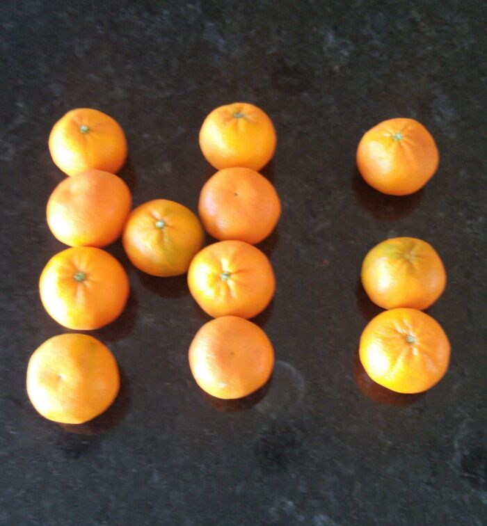 Unhinged image of oranges arranged to spell 'Hi' on a dark countertop.