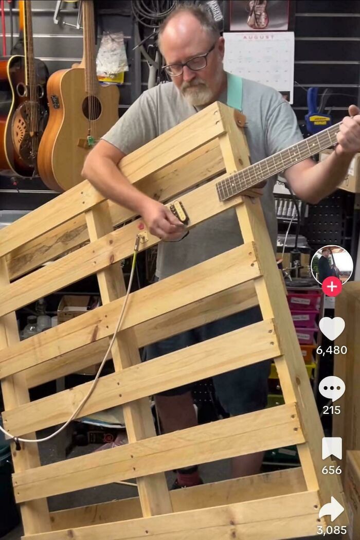 An unhinged image of a man playing a guitar built from a wooden shipping pallet, a uniquely strange instrument.