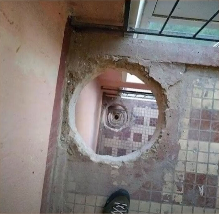 An unhinged image of a large, circular hole in a tiled floor, revealing a lower level, very unusual.