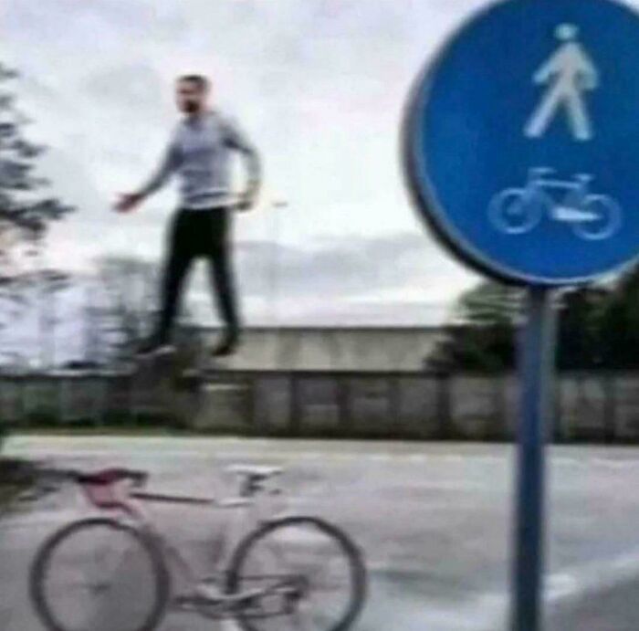 An unhinged image of a man floating above a bicycle next to a pedestrian and bike lane sign, an odd sight.