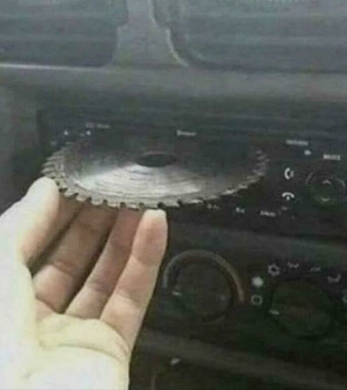 A hand holding a circular saw blade, about to insert it into a car's CD player. An unhinged image that made people go hmmm.