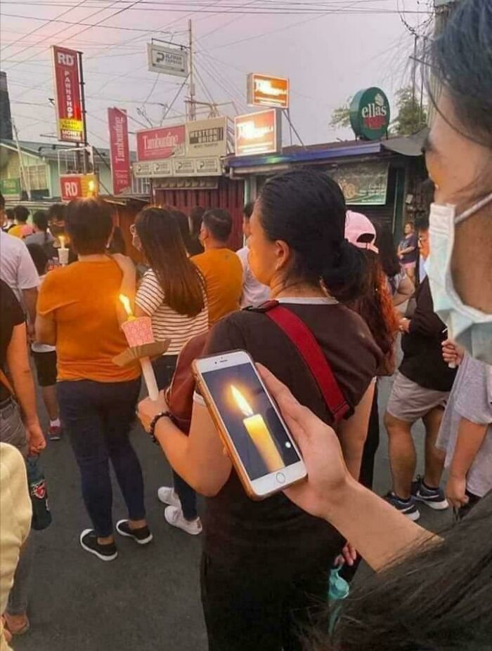 A person using a phone to display a candle light, mimicking real candles in a crowd. An unhinged image that made people go hmmm.