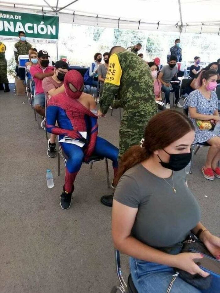 Spider-Man gets a vaccine shot in a crowded outdoor area, surrounded by people, showcasing unhinged images.
