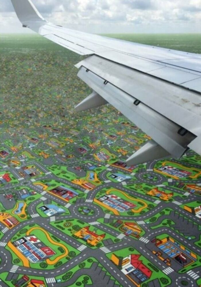 An airplane wing flies over a landscape that looks like a play mat with roads and houses, showcasing unhinged images.