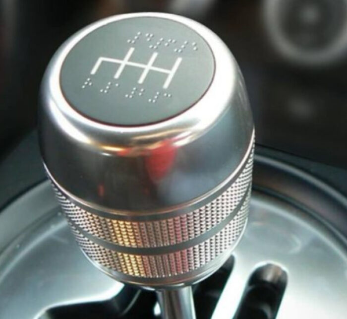 A close-up of a silver car gear shift k**b with braille markings, one of many unhinged images.